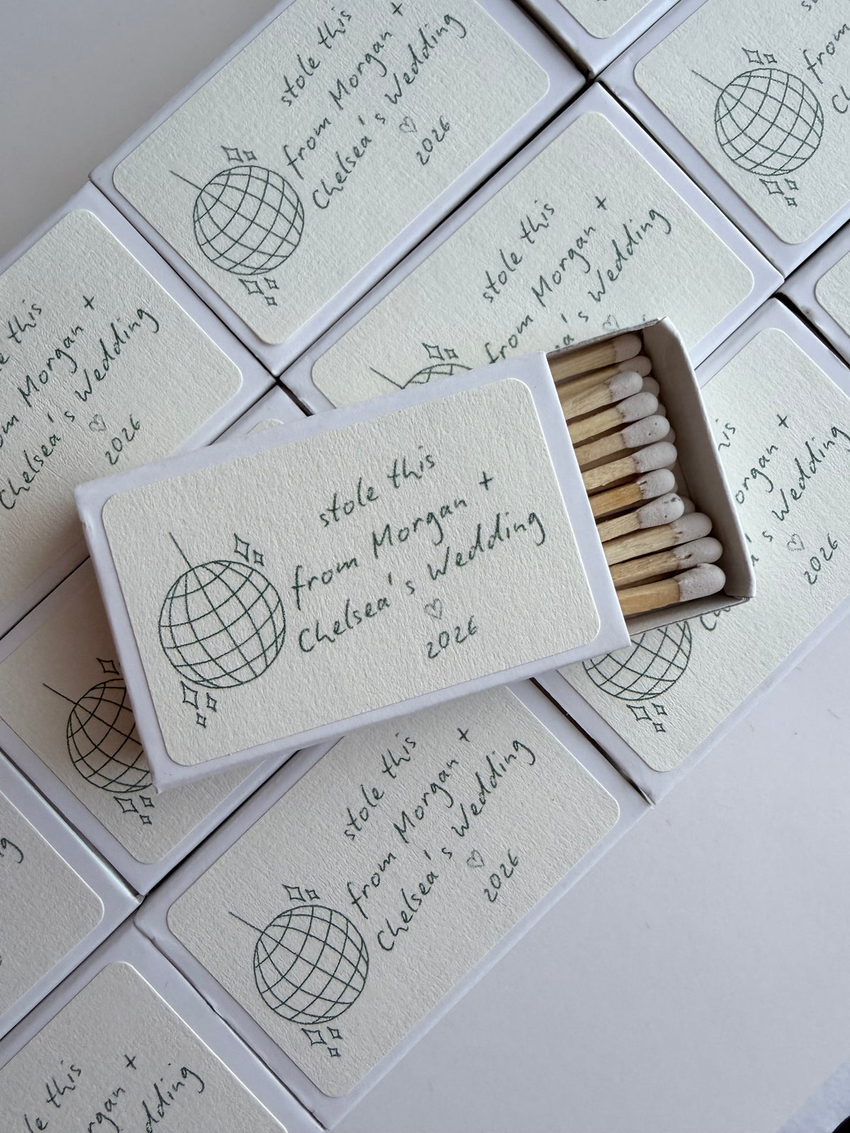 Stack of personalized disco ball wedding matchboxes with couple names, styled as wedding favors